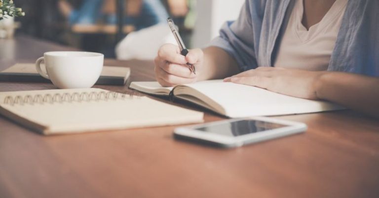 Learning - Woman Writing on a Notebook Beside Teacup and Tablet Computer
